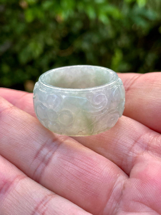 Hand holding a Size US 11.5 Grade A Burmese jadeite thumb ring featuring an intricately hand-carved floral swirl motif in icy white and imperial green, item JRN031