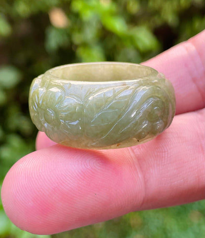 Hand holding a Size US 11 Grade A Burmese jadeite thumb ring featuring a delicate hand-carved floral swirl motif in deep mossy green, item JRN030
