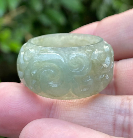 Hand holding a Size US 11.5 Grade A Burmese jadeite thumb ring featuring a hand-carved round swirl motif in icy translucent apple green, item JRN034