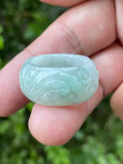 Hand holding a Size US 9 Grade A Burmese jadeite thumb ring featuring a hand-carved swirl motif in icy bluish apple green, item JRN039