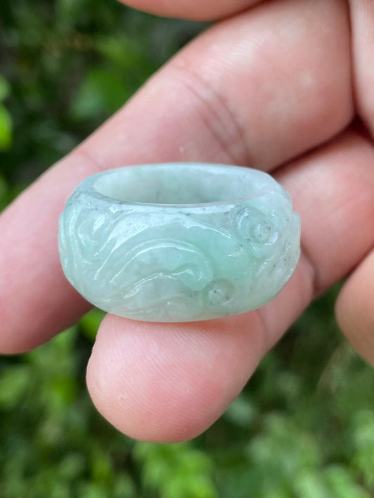 Hand holding a Size US 9 Grade A Burmese jadeite thumb ring featuring a hand-carved swirl motif in icy bluish apple green, item JRN039