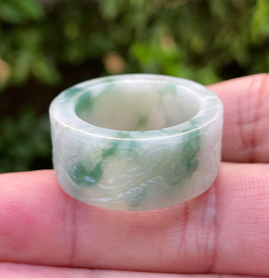 Hand holding a Size US 12 Grade A Burmese jadeite thumb ring featuring an elegantly hand-carved swirl motif in icy imperial green and milky white, item JRN026