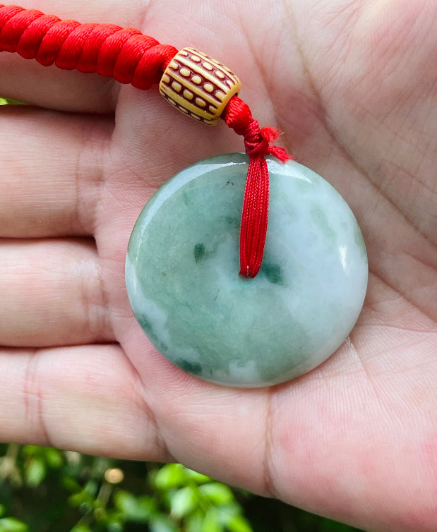 Untreated Type A Burmese jade pendant showing semi-gloss luster with beautiful green and white colors on a vivid red adjustable cord