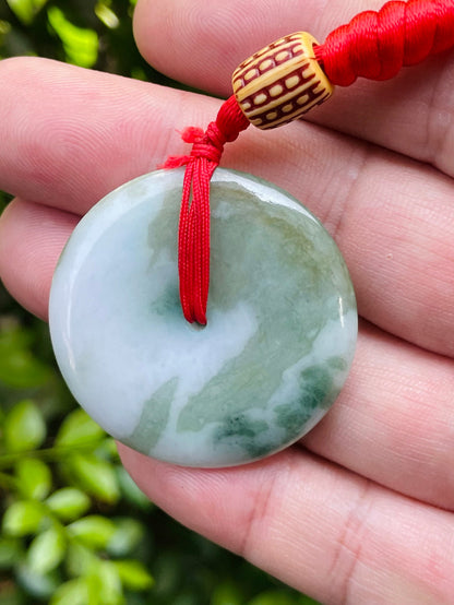 Untreated Type A Burmese jade pendant showing semi-gloss luster with beautiful green and white colors on a vivid red adjustable cord