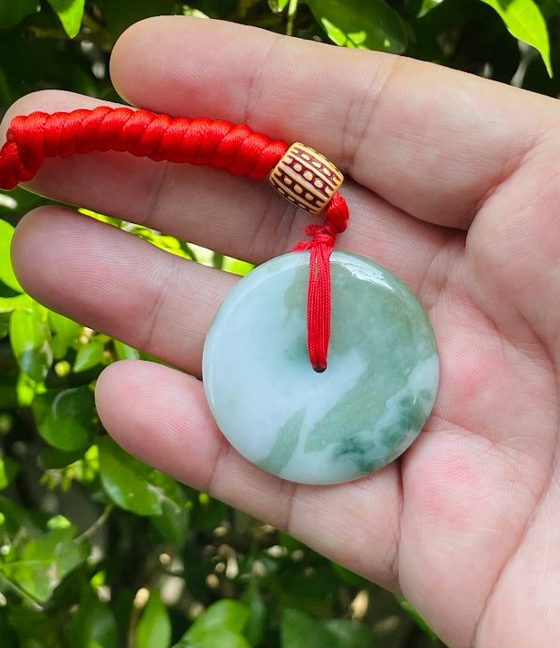 Untreated Type A Burmese jade pendant showing semi-gloss luster with beautiful green and white colors on a vivid red adjustable cord