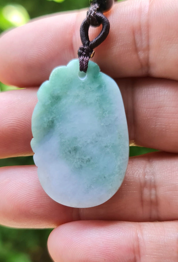 Untreated Type A Burmese jade pendant showing semi-translucent luster with beautiful green and white colors on a dark brown woven cord