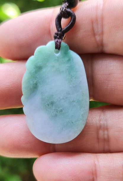 Untreated Type A Burmese jade pendant showing semi-translucent luster with beautiful green and white colors on a dark brown woven cord