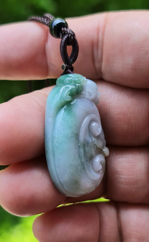 Untreated Type A Burmese jade pendant showing semi-translucent luster with beautiful green and white colors on a dark brown woven cord