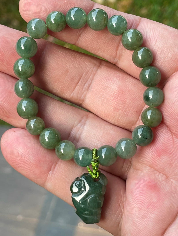 8.2mm natural Type A Burmese jade beads showing soft translucency, icy deep mossy green hues, and a hand-carved Pixiu pendant on the wrist