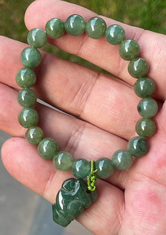 8.2mm natural Type A Burmese jade beads showing soft translucency, icy deep mossy green hues, and a hand-carved Pixiu pendant on the wrist