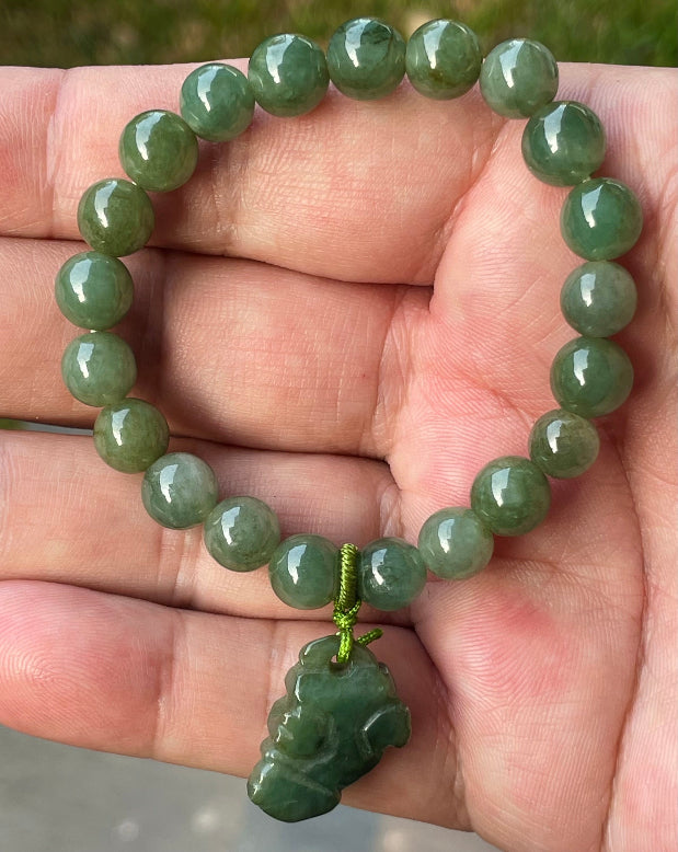 8.2mm natural Type A Burmese jade beads showing soft translucency, icy deep mossy green hues, and a hand-carved Pixiu pendant on the wrist
