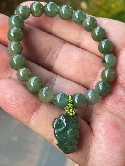 8.2mm natural Type A Burmese jade beads showing soft translucency, icy deep mossy green hues, and a hand-carved Pixiu pendant on the wrist
