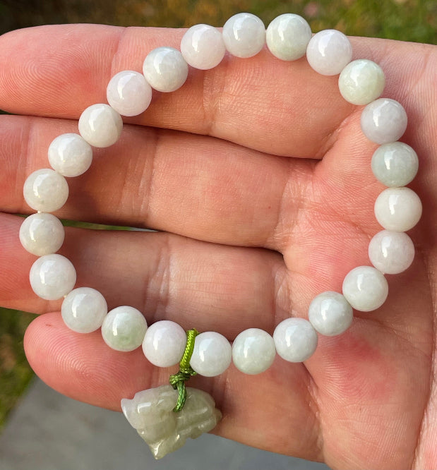 8mm natural Type A Burmese jade beads showing gentle translucency, milky white and pale green hues, and a hand-carved tiger pendant on the wrist