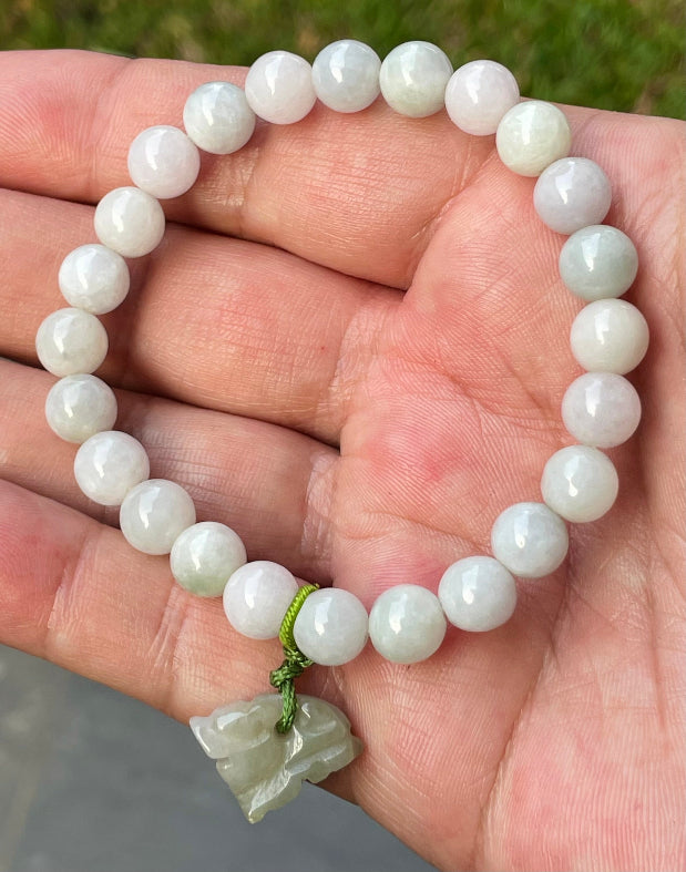 8mm natural Type A Burmese jade beads showing gentle translucency, milky white and pale green hues, and a hand-carved tiger pendant on the wrist