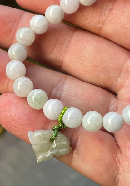 8mm natural Type A Burmese jade beads showing gentle translucency, milky white and pale green hues, and a hand-carved tiger pendant on the wrist