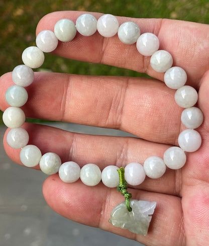 8mm natural Type A Burmese jade beads showing gentle translucency, milky white and pale green hues, and a hand-carved tiger pendant on the wrist