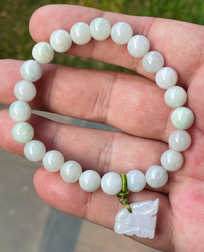 8mm natural Type A Burmese jade beads showing gentle translucency, white and icy green hues, and a hand-carved tiger pendant on the wrist