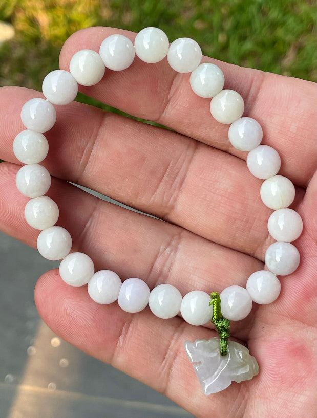 7.8mm natural Type A Burmese jade beads showing gentle translucency, white and lavender hues, and a hand-carved tiger pendant on the wrist