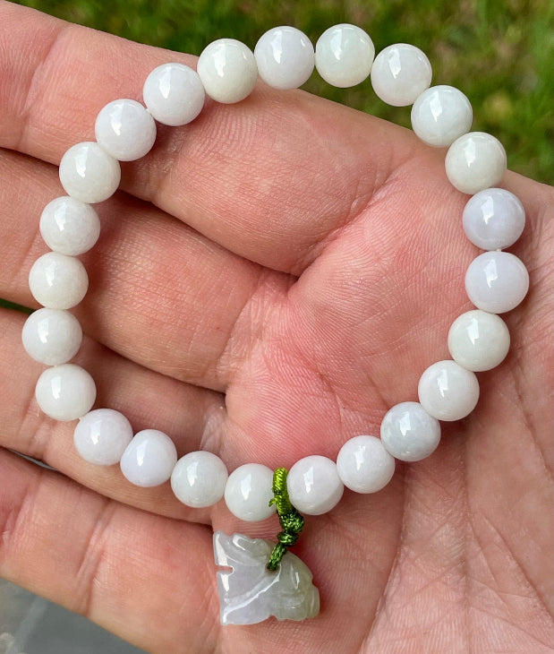 7.8mm natural Type A Burmese jade beads showing gentle translucency, white and lavender hues, and a hand-carved tiger pendant on the wrist