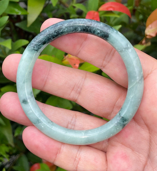 Close-up of a 57mm natural Grade A Burmese jadeite bangle featuring bluish apple green and black hues, item JB943