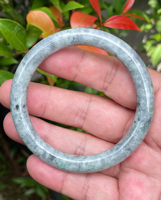 Close-up of a 58.6mm natural Grade A Burmese jadeite bangle featuring gray and milky white hues with black inclusions, item JB947