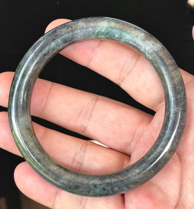 Close-up of a 62.2mm natural Grade A Burmese jadeite bangle featuring icy black, grayish milky white, and bluish green hues, item JB409