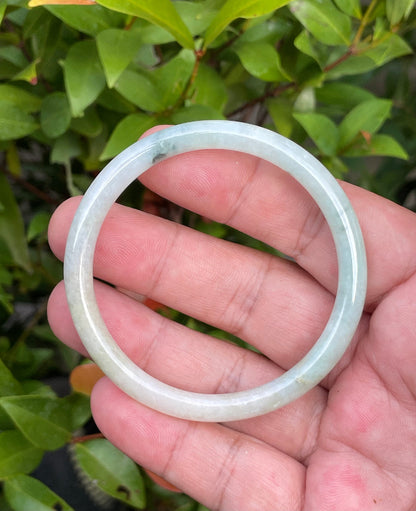 Close-up of a 54.7mm natural Grade A Burmese jadeite bangle featuring icy milky white, bluish green, and yellow hues, item JB753