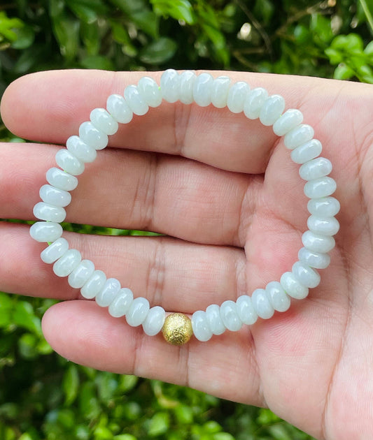 Close-up of a 7.7mm natural Grade A Burmese jadeite beaded bracelet featuring icy apple green donut-shaped rondelles and a gold accent bead, item JBB166