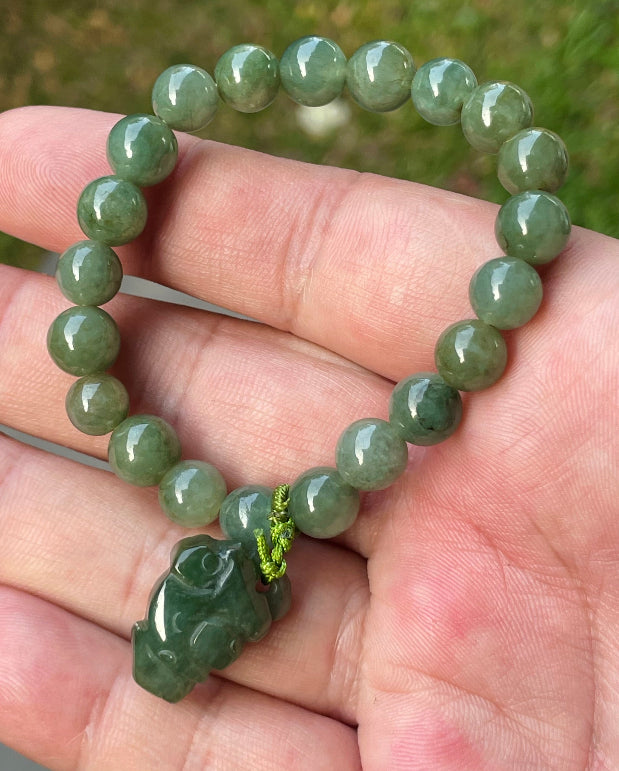 Handcrafted genuine Grade A Burmese jadeite stretch bracelet showcasing beautiful icy deep mossy green beads with a hand-carved Pixiu pendant