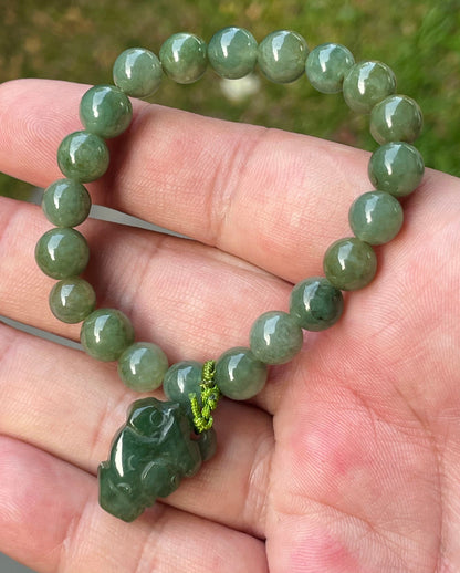 Handcrafted genuine Grade A Burmese jadeite stretch bracelet showcasing beautiful icy deep mossy green beads with a hand-carved Pixiu pendant