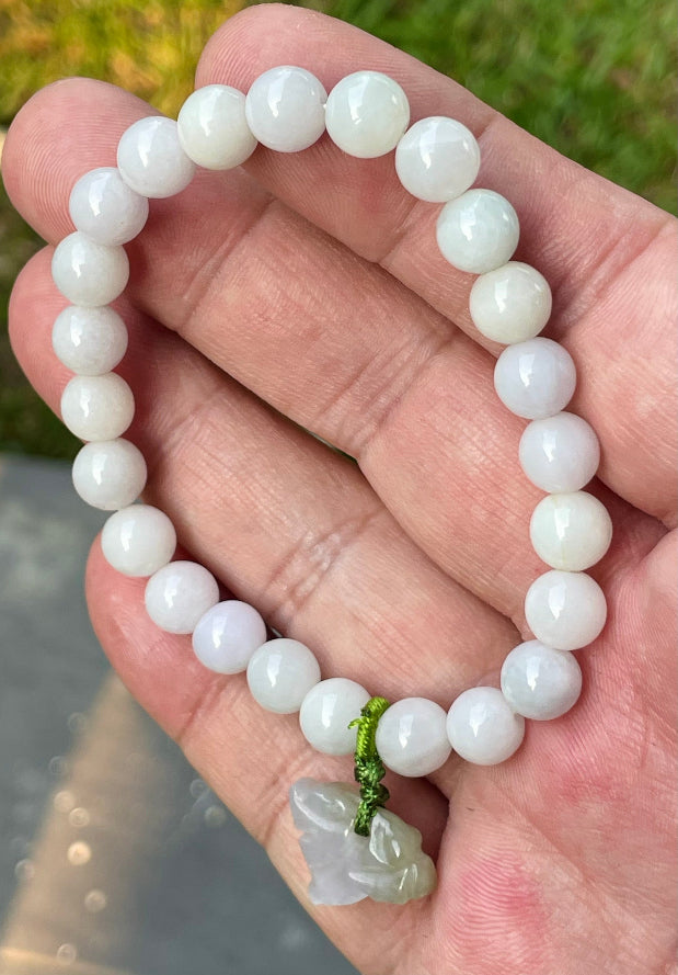 Handcrafted genuine Grade A Burmese jadeite stretch bracelet showcasing beautiful milky white and light lavender beads with a hand-carved tiger pendant