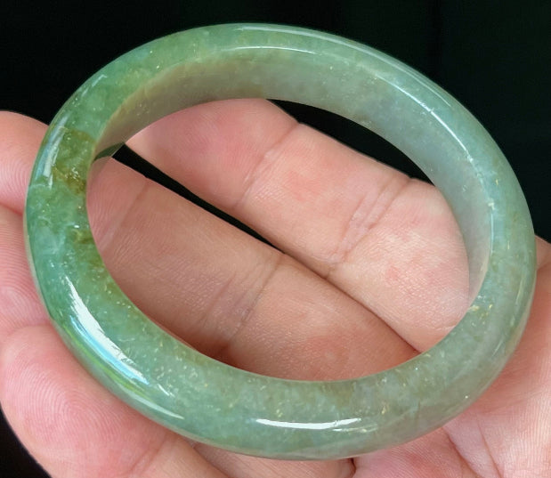 Close-up of forest green and honey hues on icy apple green jadeite bangle