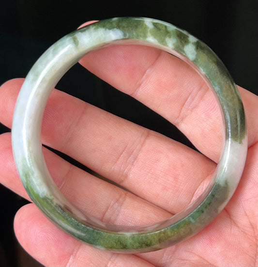 Hand holding a 57.2mm natural Grade A Burmese jadeite bangle in icy apple and forest green with milky white hues, item JB517