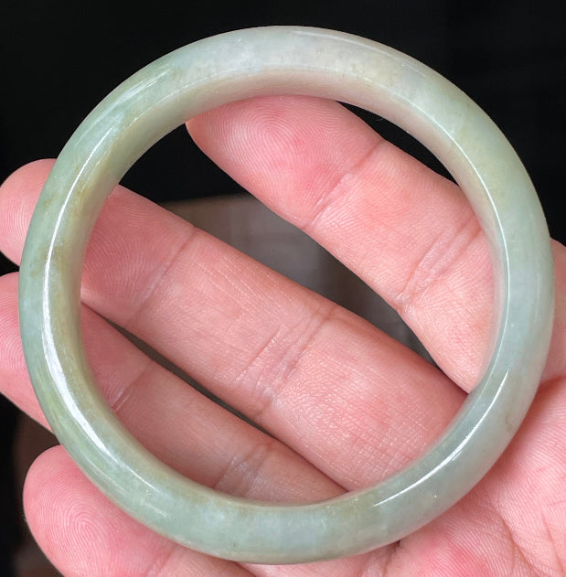 Hand holding a 57.3mm natural Grade A Burmese jadeite bangle in icy apple green, item JB073