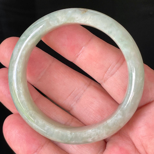 Hand holding a 50.8mm natural Grade A Burmese jadeite bangle in icy apple green and milky white hues, item JB238