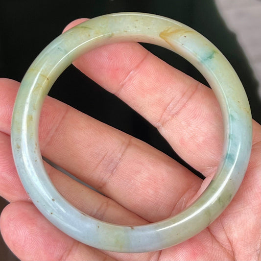 Hand holding a 58.7mm natural Grade A Burmese jadeite bangle in icy apple and imperial green with honey hues, item JB528