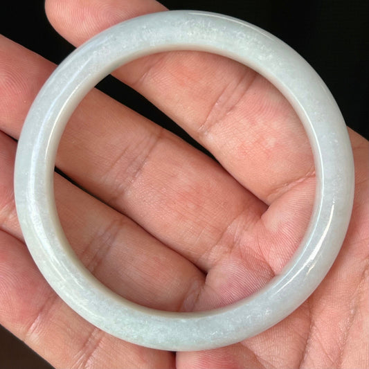 Hand holding a 55.3mm natural Grade A Burmese jadeite bangle in icy grey and milky white, item JB542