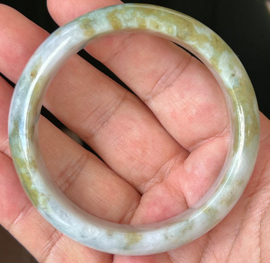 Hand holding a 57.2mm natural Grade A Burmese jadeite bangle in icy grey and milky white with apple moss green, item JB523