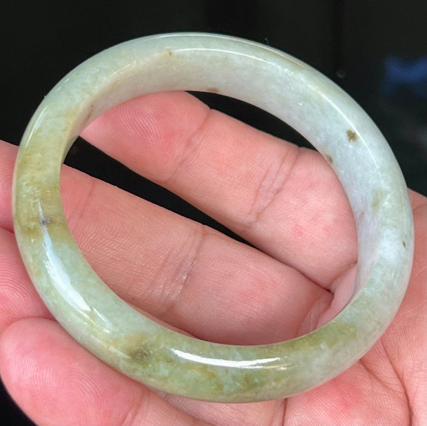 Close-up of apple green and honey hues on icy greyish white jadeite bangle