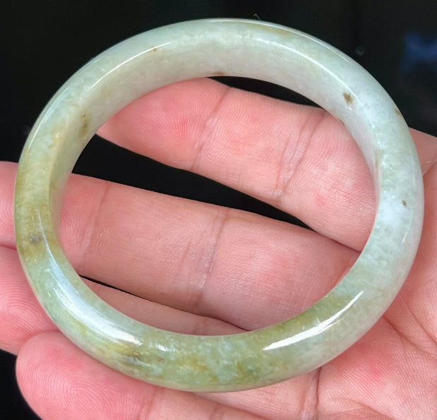 Close-up of apple green and honey hues on icy greyish white jadeite bangle