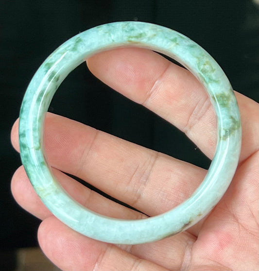 Hand holding a 58.5mm natural Grade A Burmese jadeite bangle in icy imperial and apple green with milky white and honey, item JB553