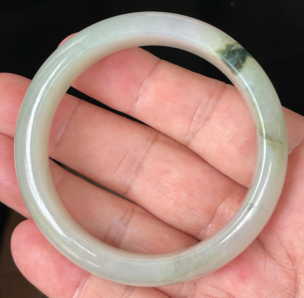 Hand holding a 55mm natural Grade A Burmese jadeite bangle in icy light apple and forest green hues, item JB074