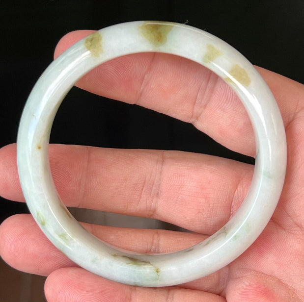 Hand holding a 58.5mm natural Grade A Burmese jadeite bangle in icy milky white with moss and apple green hues, item JB552