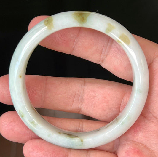 Hand holding a 58.5mm natural Grade A Burmese jadeite bangle in icy milky white with moss and apple green hues, item JB552