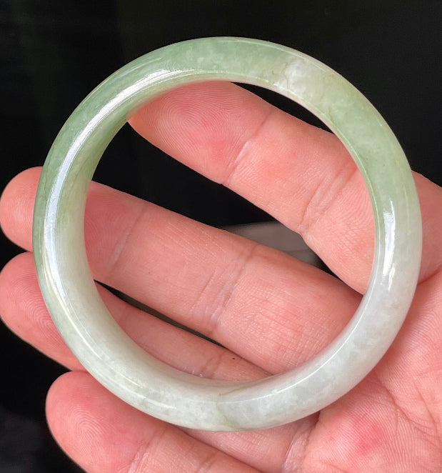 Hand holding a 56.6mm natural Grade A Burmese jadeite bangle in icy milky white and apple green, item JB151