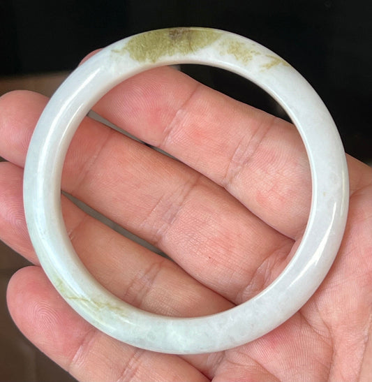 Hand holding a 58.4mm natural Grade A Burmese jadeite bangle in icy milky white with forest green hues, item JB508
