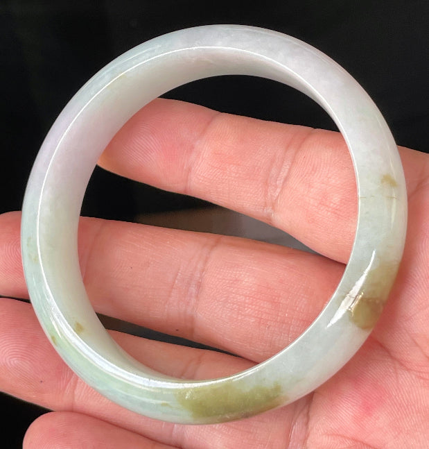 Hand holding a 58.7mm natural Grade A Burmese jadeite bangle in icy milky white with light apple green, forest green, and lavender hues, item JB226