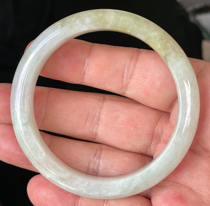 Hand holding a 58.8mm natural Grade A Burmese jadeite bangle in icy milky white with light apple green hues, item JB237