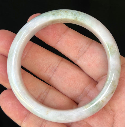Hand holding a 58.6mm natural Grade A Burmese jadeite bangle in icy milky white with apple and forest green, item JB502