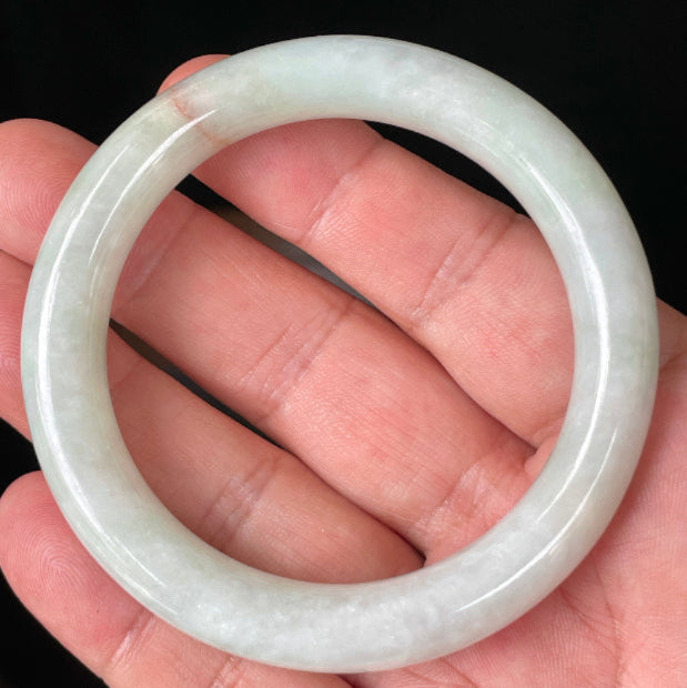 Hand holding a 55.8mm natural Grade A Burmese jadeite bangle in icy milky white and apple green with an orange line, item JB157
